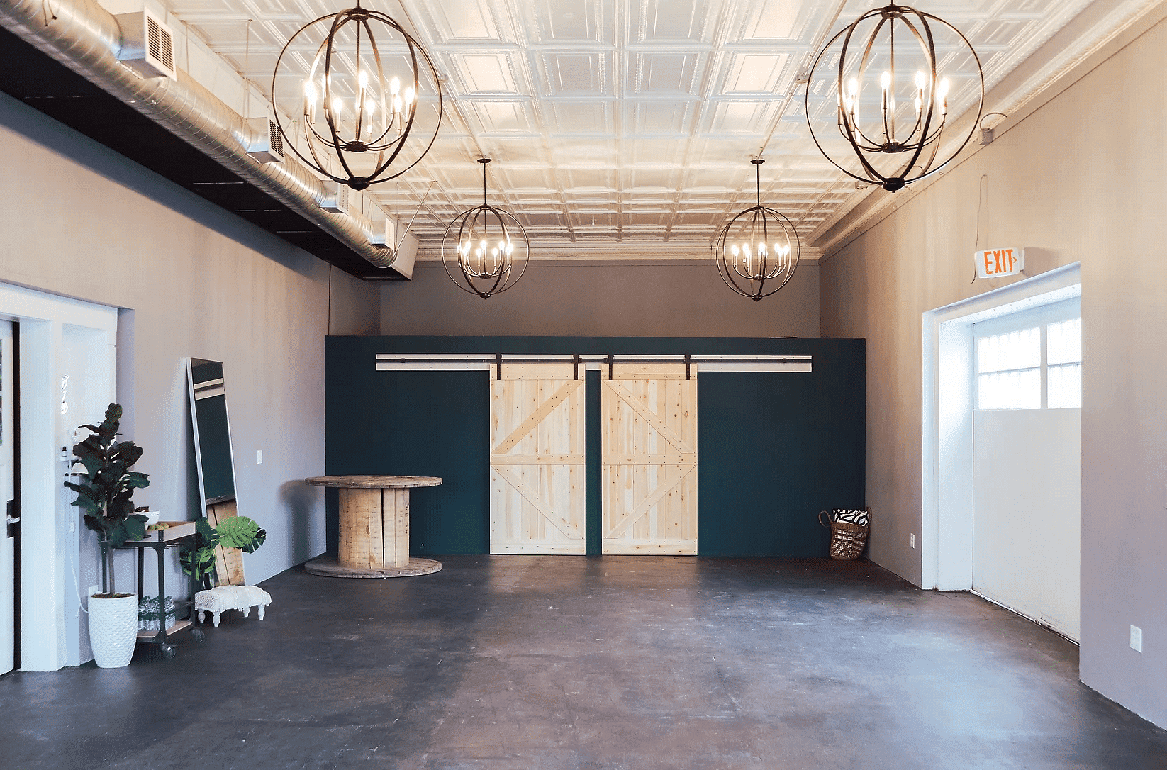 Empty industrial-style room with large chandeliers and wooden doors.