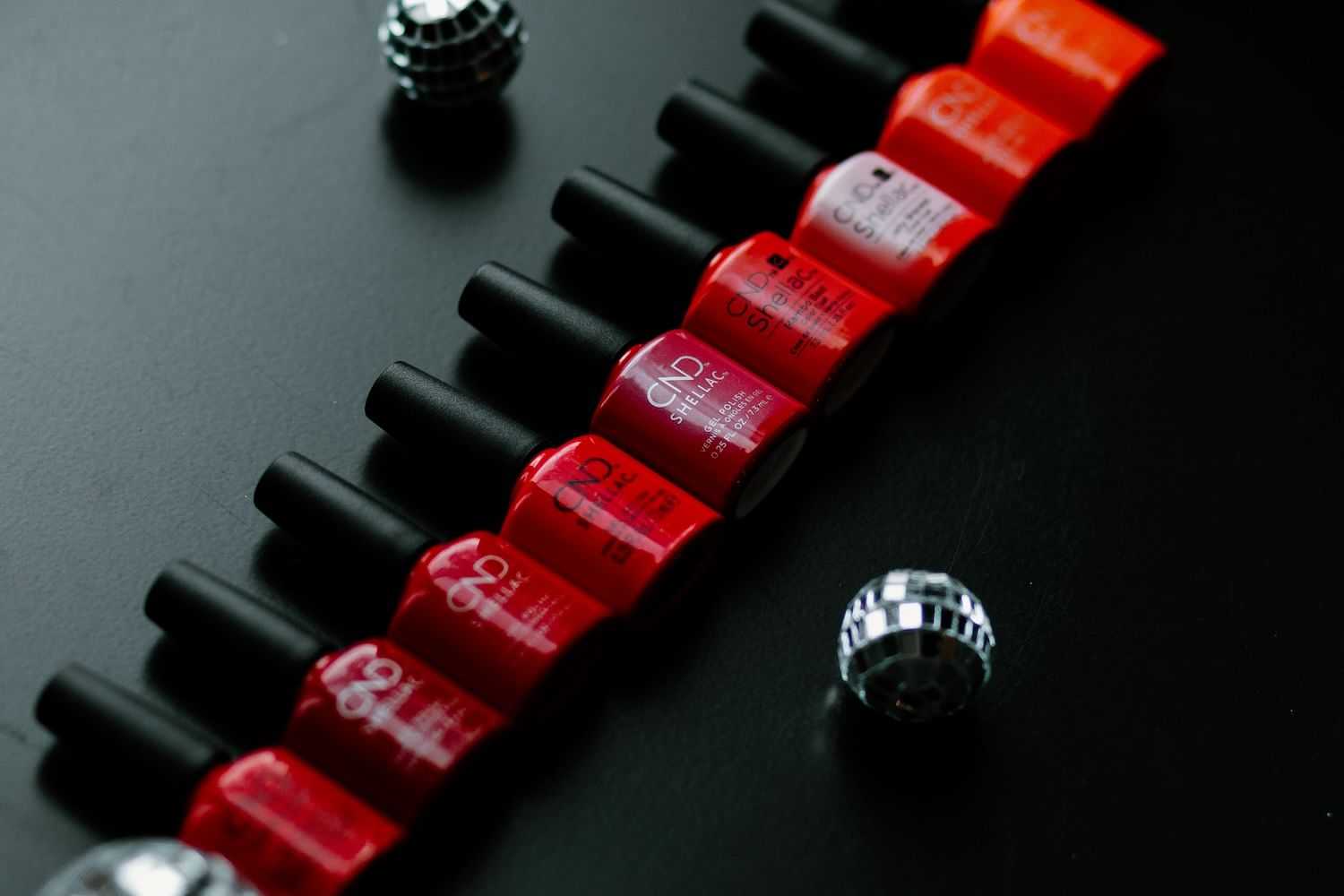 Row of red nail polish bottles on a black surface.