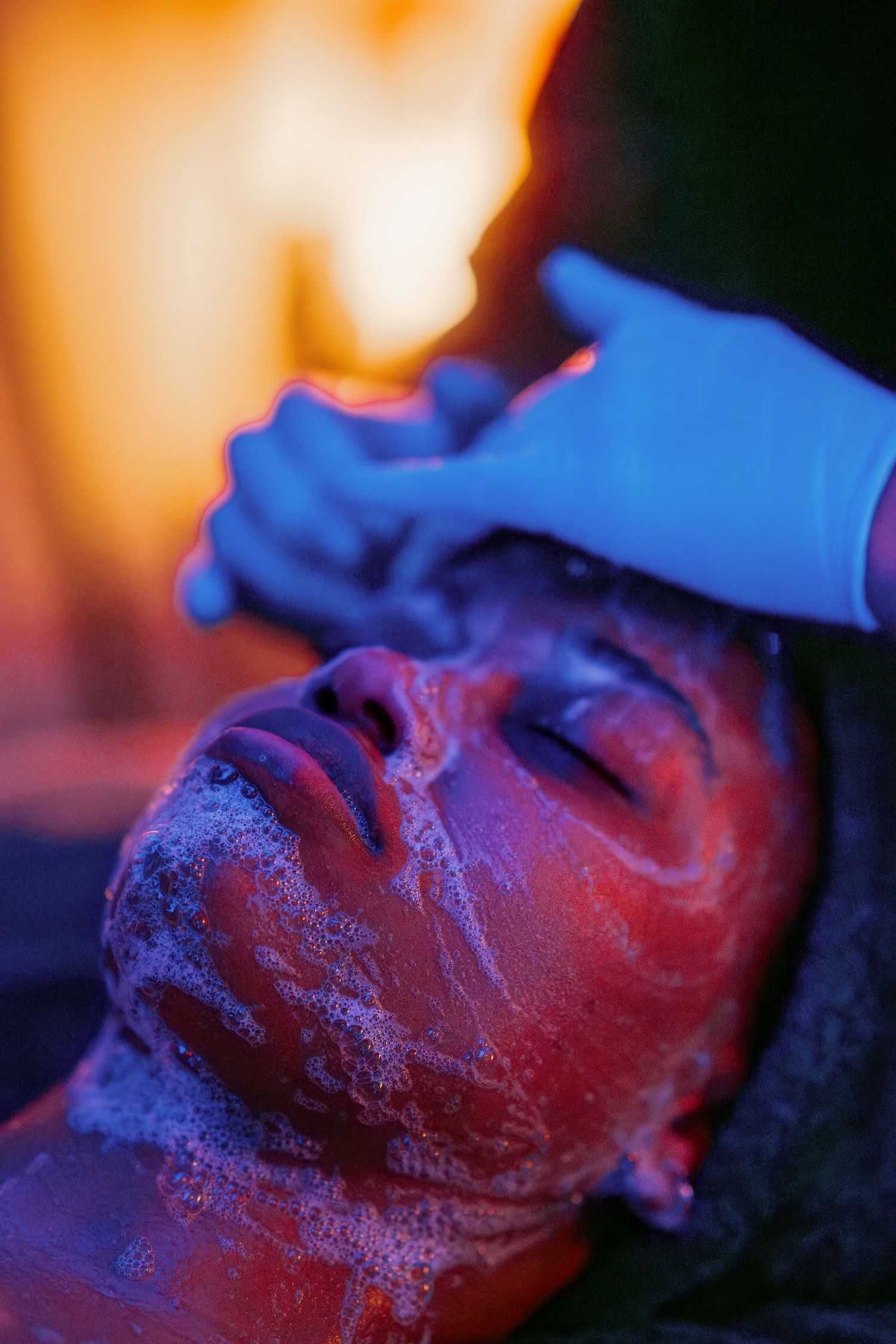 Person receiving a facial treatment under colorful lighting.