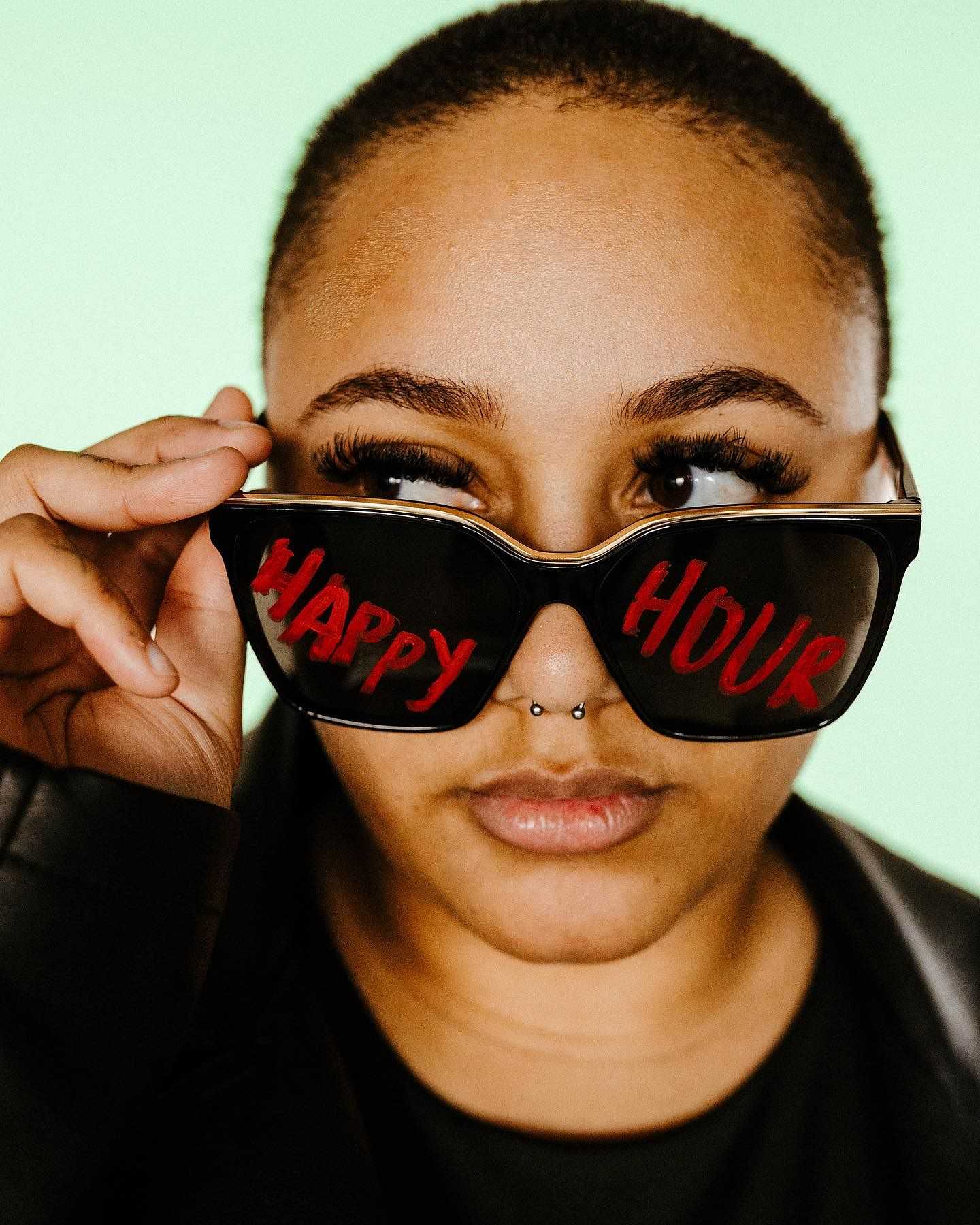 Woman wearing sunglasses with "Happy Hour" text on them.