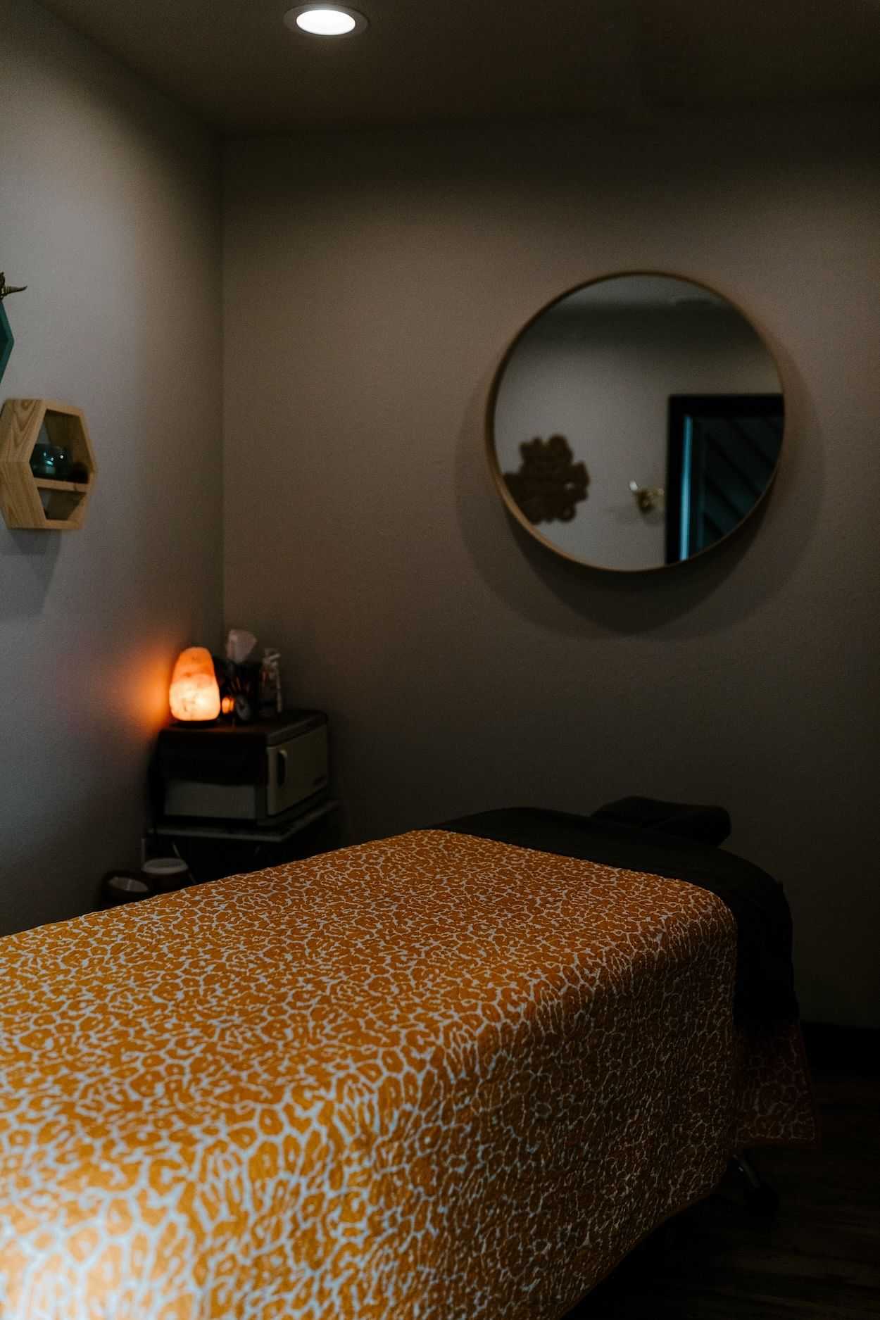 A cozy massage room with a leopard print bed cover and a round mirror.