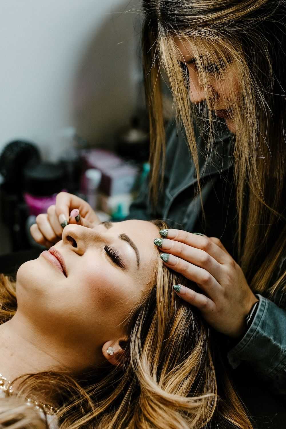 Makeup artist applying eyeliner to a reclined woman in a salon.