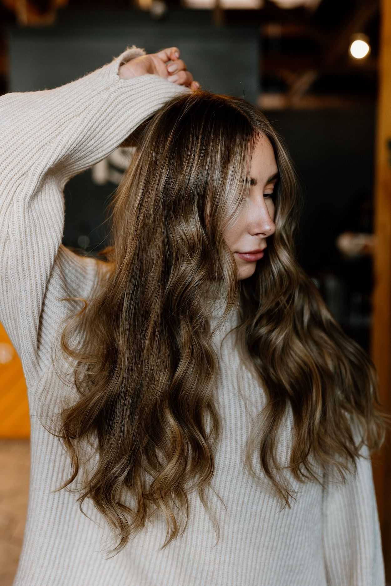 Woman with long wavy hair posing in a cozy indoor setting.